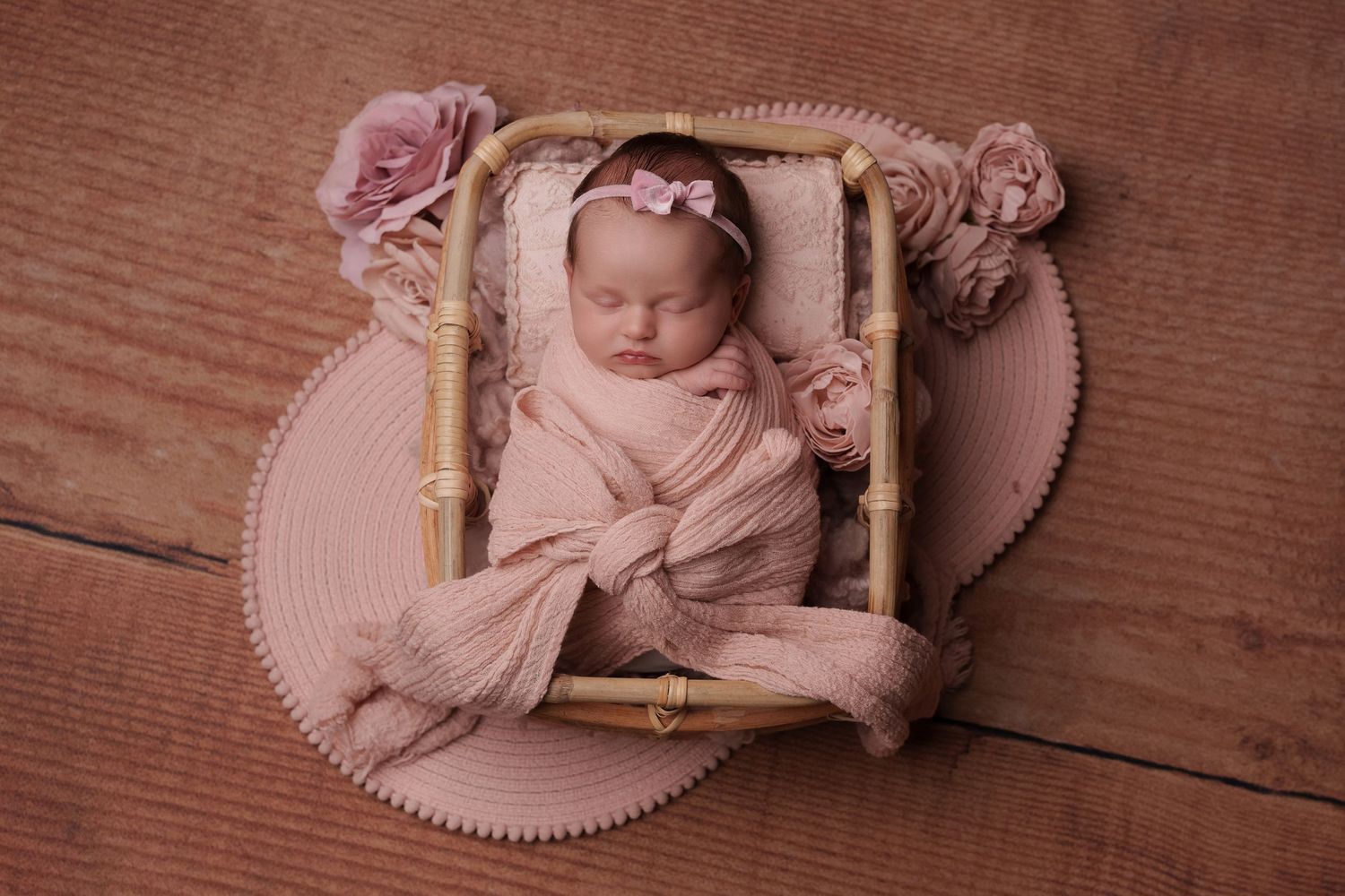 Peaceful newborn wrapped in fabric within ornate frame surrounded by pink roses.