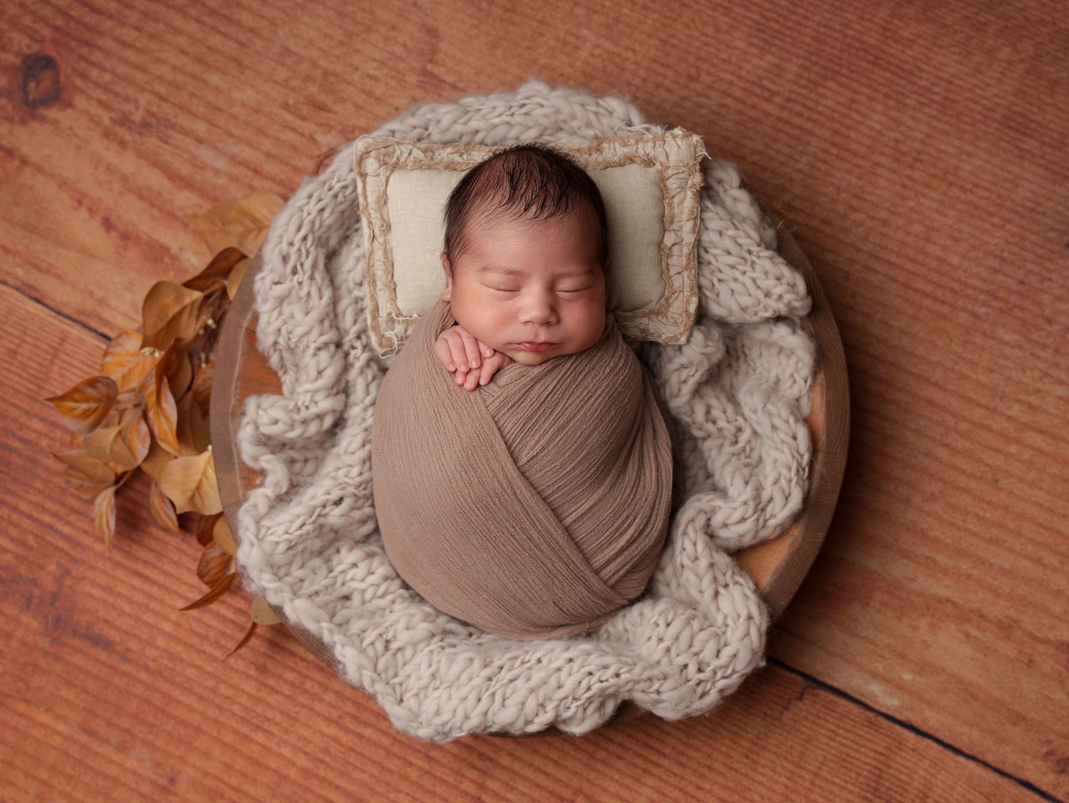 Newborn wrapped in tan swaddle sleeping on chunky knit blanket.