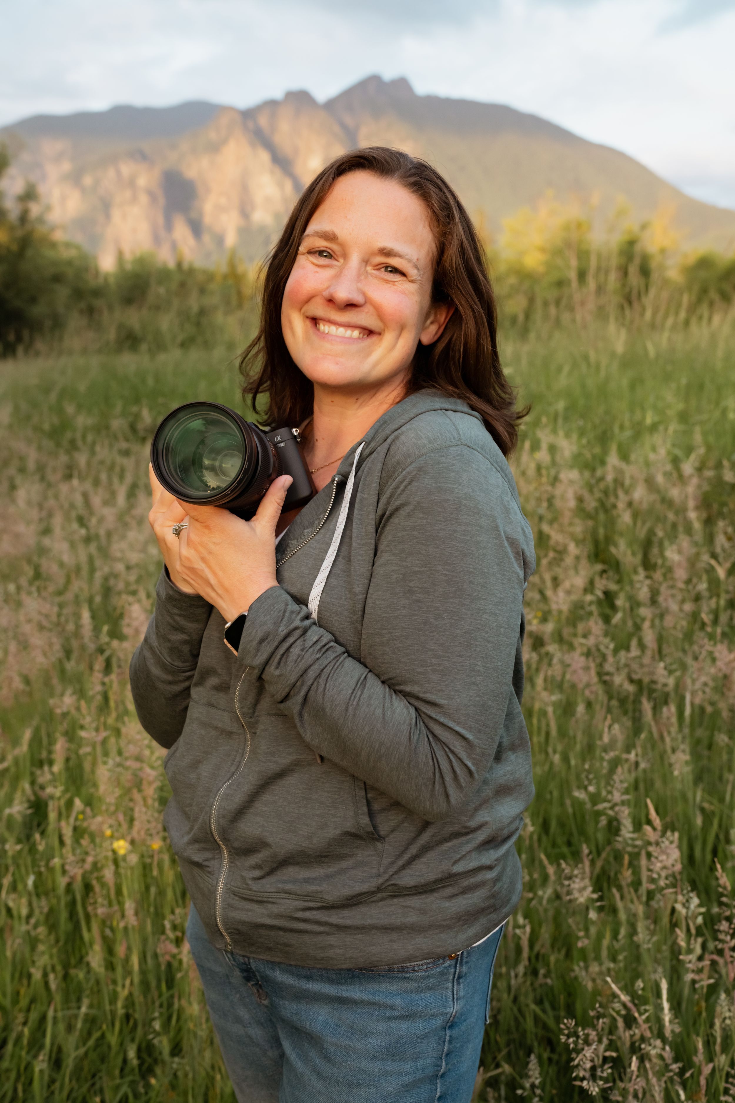 Photographer in floral dress holding camera in field of wildflowers at golden hour.
