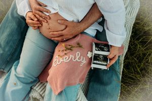 Close-up of pregnant belly with Averly name sweater and ultrasound photos during maternity session.