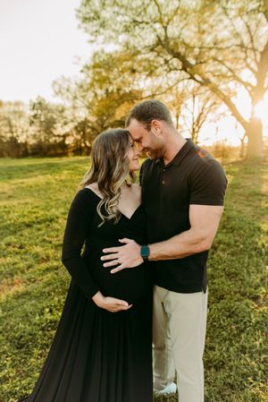 Couple touching foreheads tenderly, man holding pregnant womans baby bump at sunset in field.