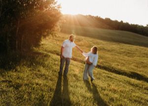 Couple holding hands and dancing in open green field bathed in beautiful golden sunset light.