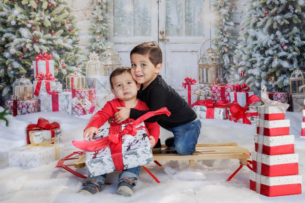 Holiday photo sample of Two young boys pose with Christmas gifts and decorated trees in a festive holiday photo session with snow decor.