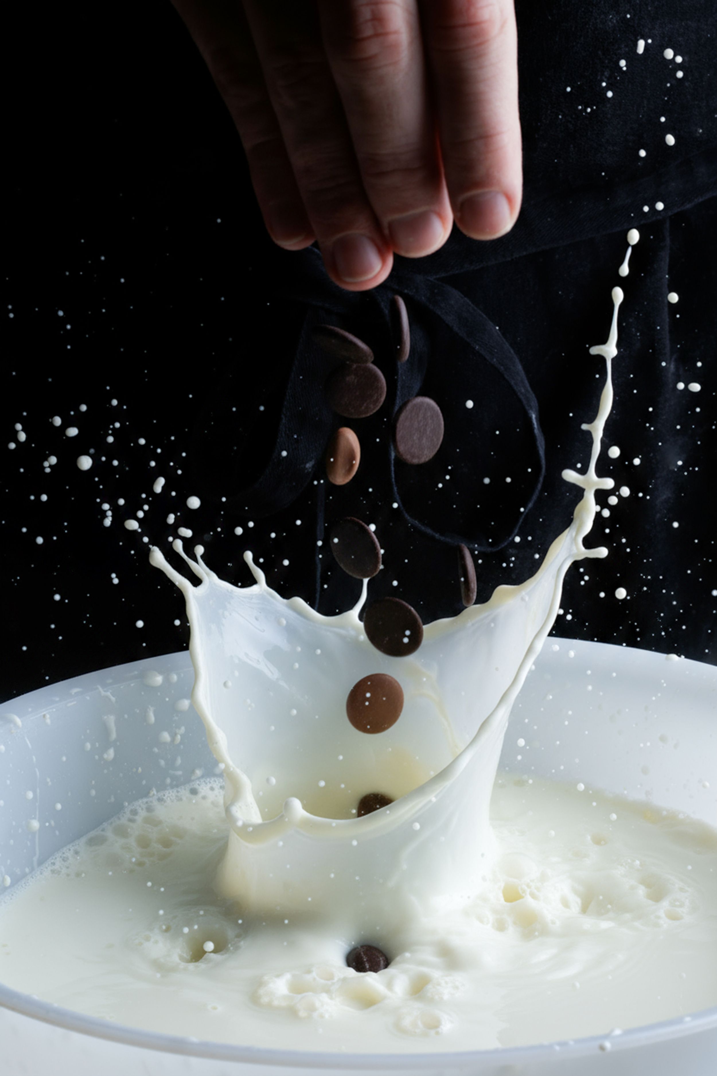 Chocolate cookies dropping into a bowl of milk creating a dramatic white splash against dark background.