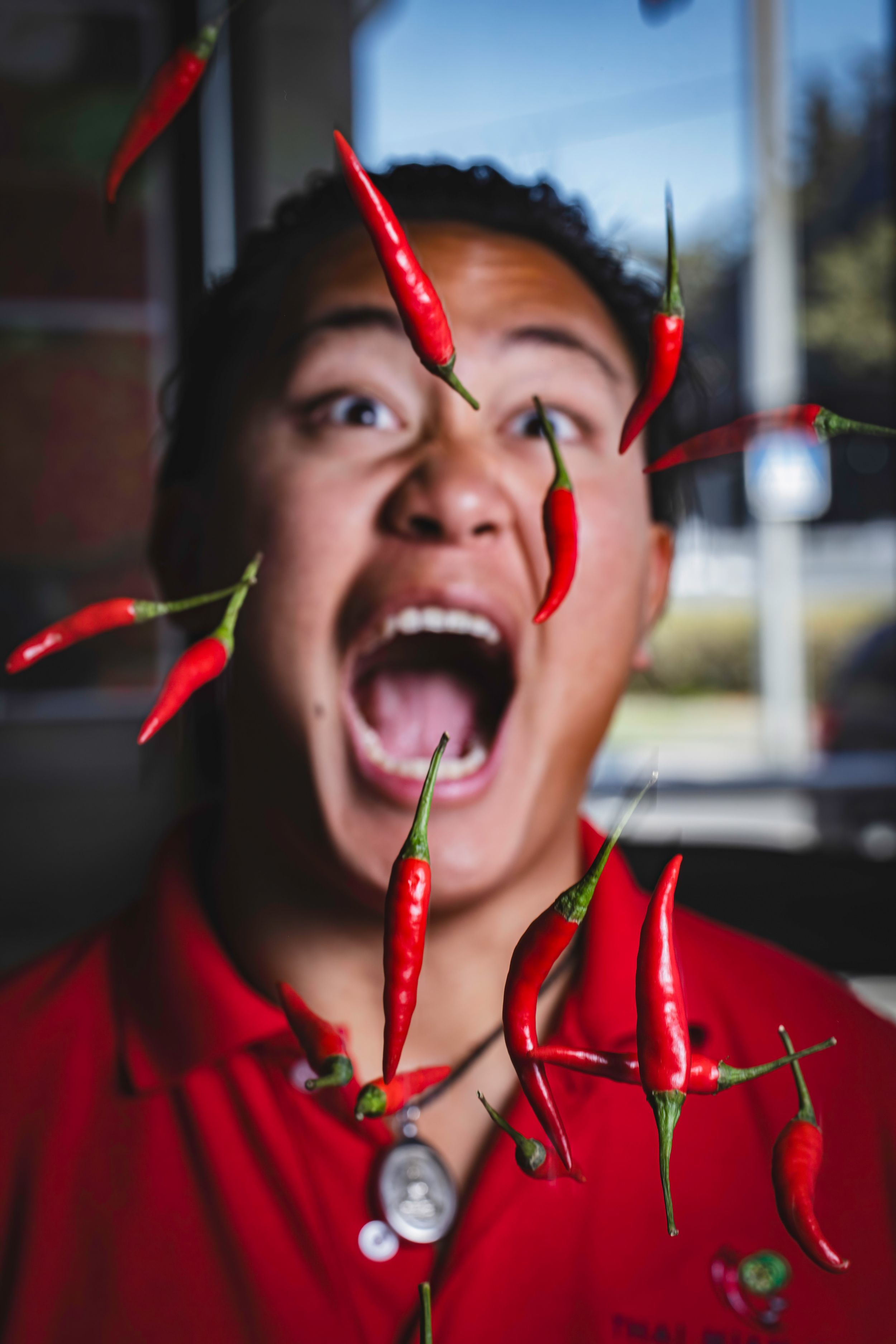 Man in red shirt reacting with open mouth as red chili peppers fly toward his face.