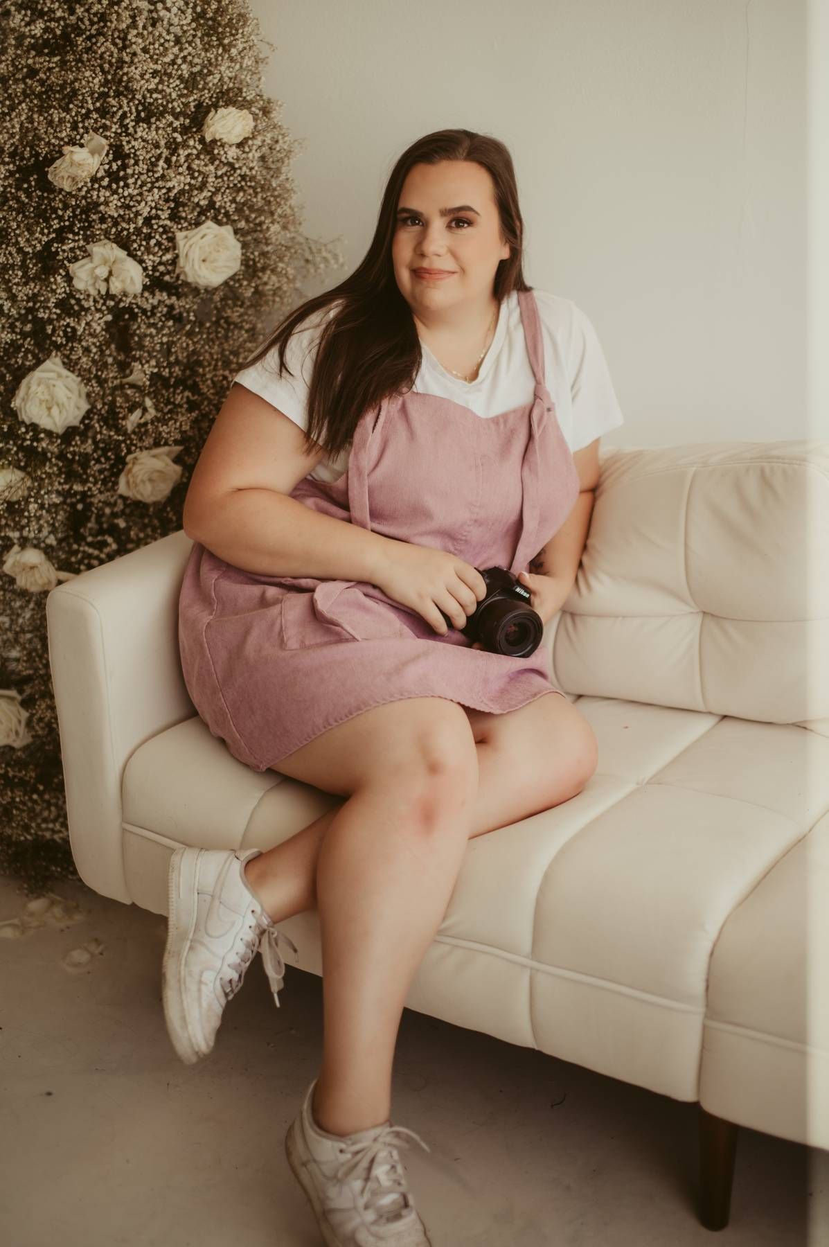Woman in pink overalls sitting on white couch next to decorated Christmas tree.