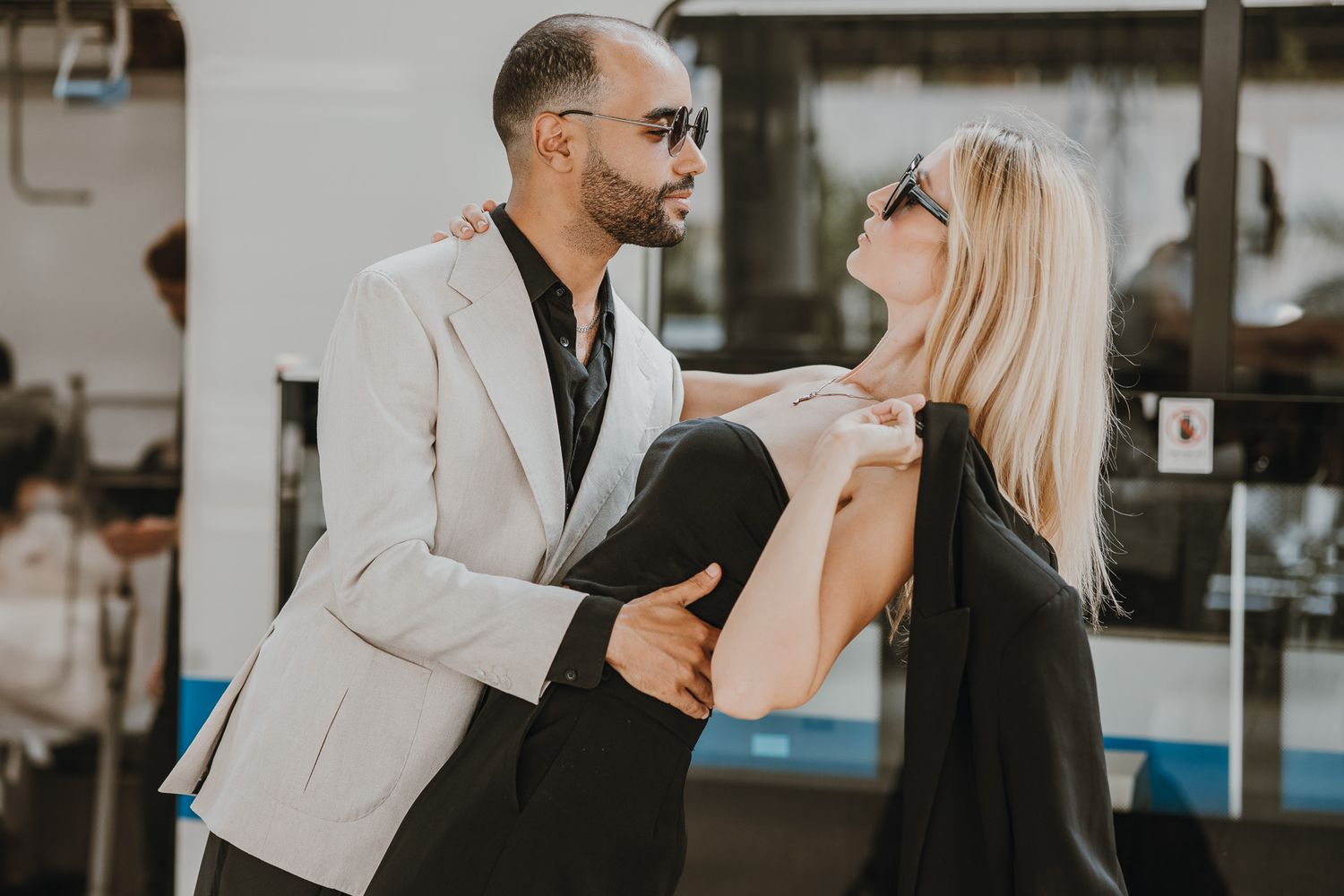 A couple dancing together in an intimate pose on a sunlit street with one person dipping their partner backward.