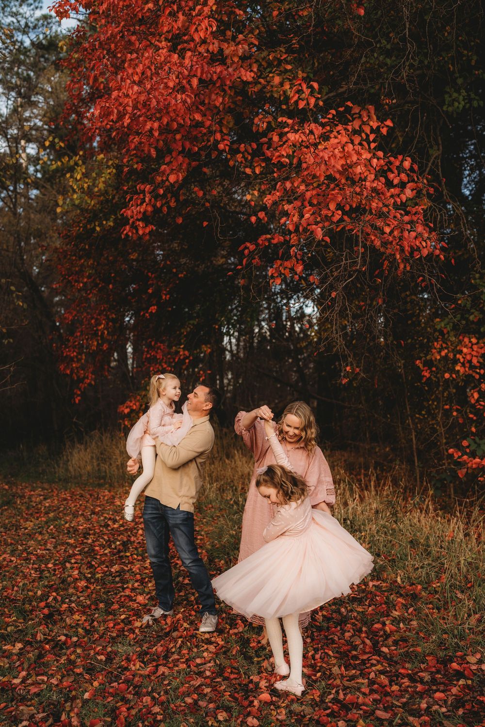 Family playing joyfully among vibrant red autumn leaves in a colorful fall forest.
