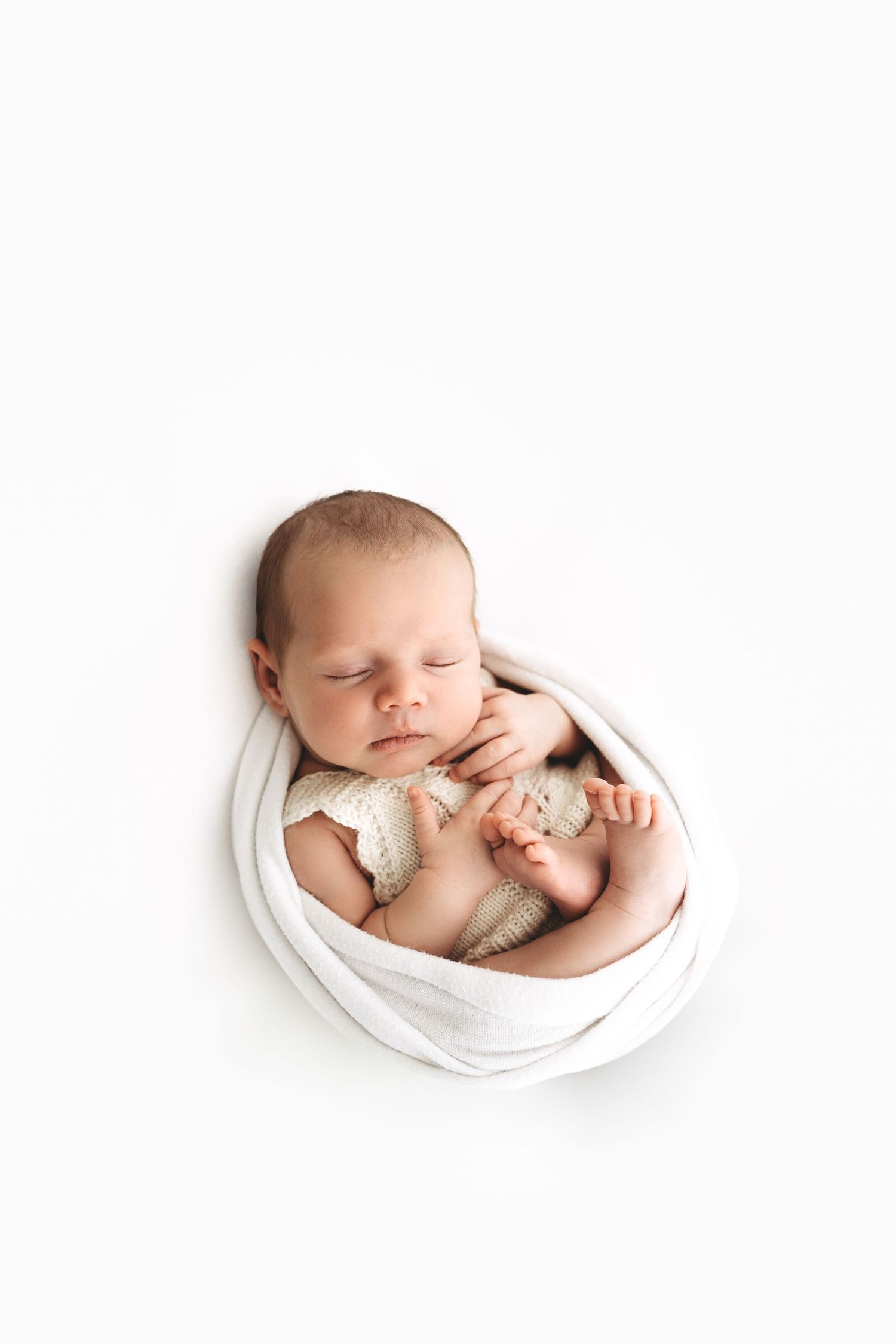 Peaceful newborn baby sleeping swaddled in white wrap holding a small knit toy.