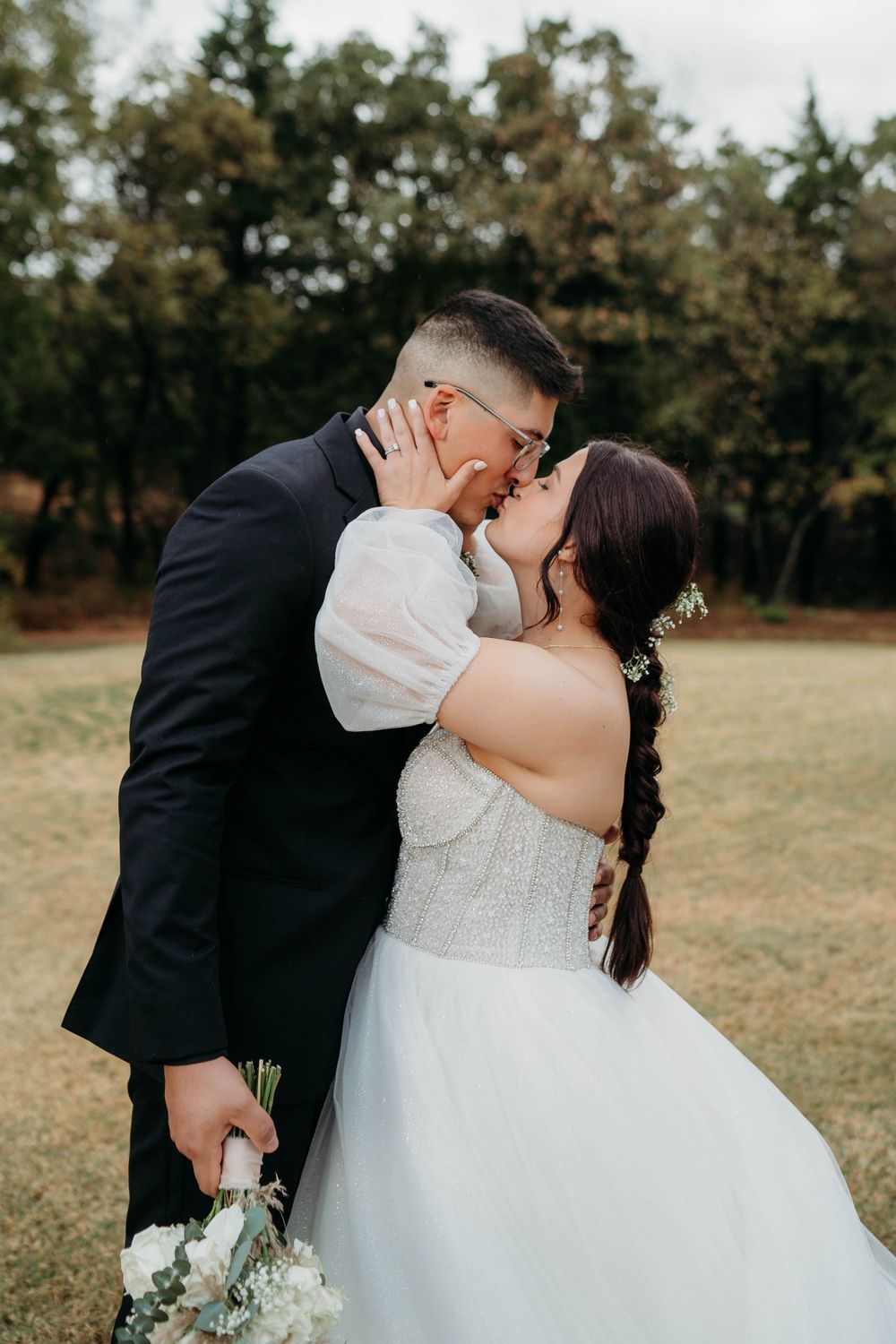Intimate wedding moment captured outdoors with white dress and dark suit.