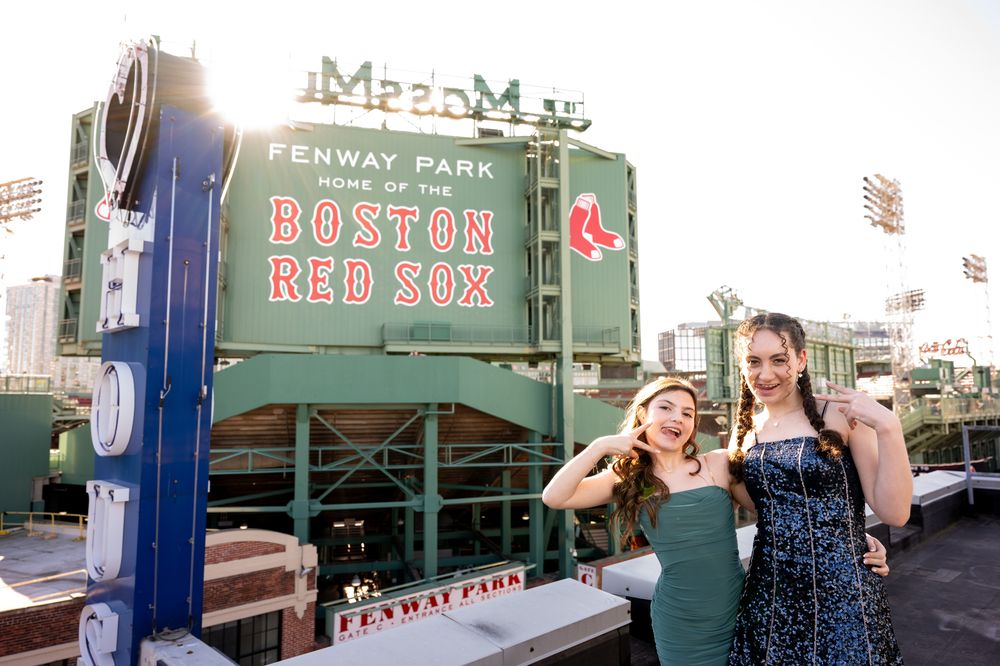 Two women posing at Fenway Park, home of the Boston Red Sox, in front of the iconic green scoreboard.