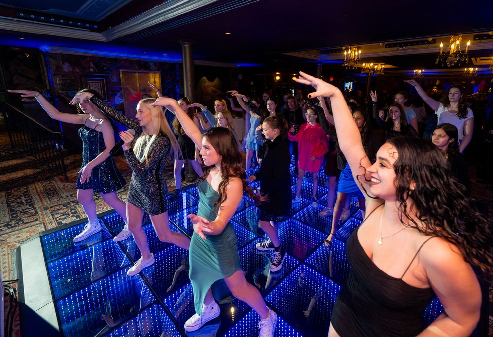 Young women dancing energetically on a illuminated blue dance floor at a lively party or nightclub event.