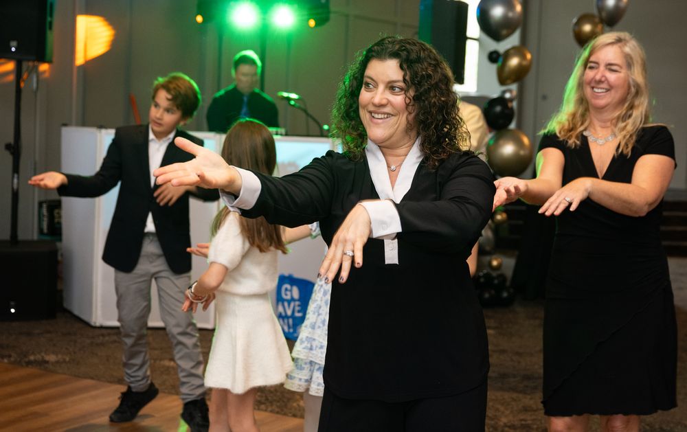 Group of adults and children dancing joyfully at an elegant party event with green stage lighting.