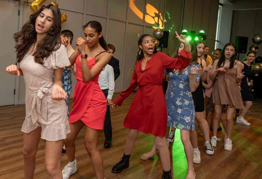 Young women dancing energetically at a party event with colorful green lights in the background.
