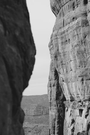 Black and white view of towering sandstone cliffs with natural rock formations in a desert landscape.