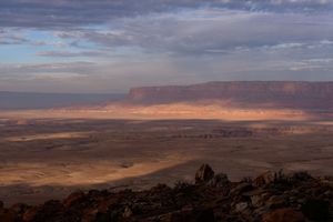 A panoramic view of the desert landscape at sunset with dramatic clouds and distant mountains stretching across the horizon.