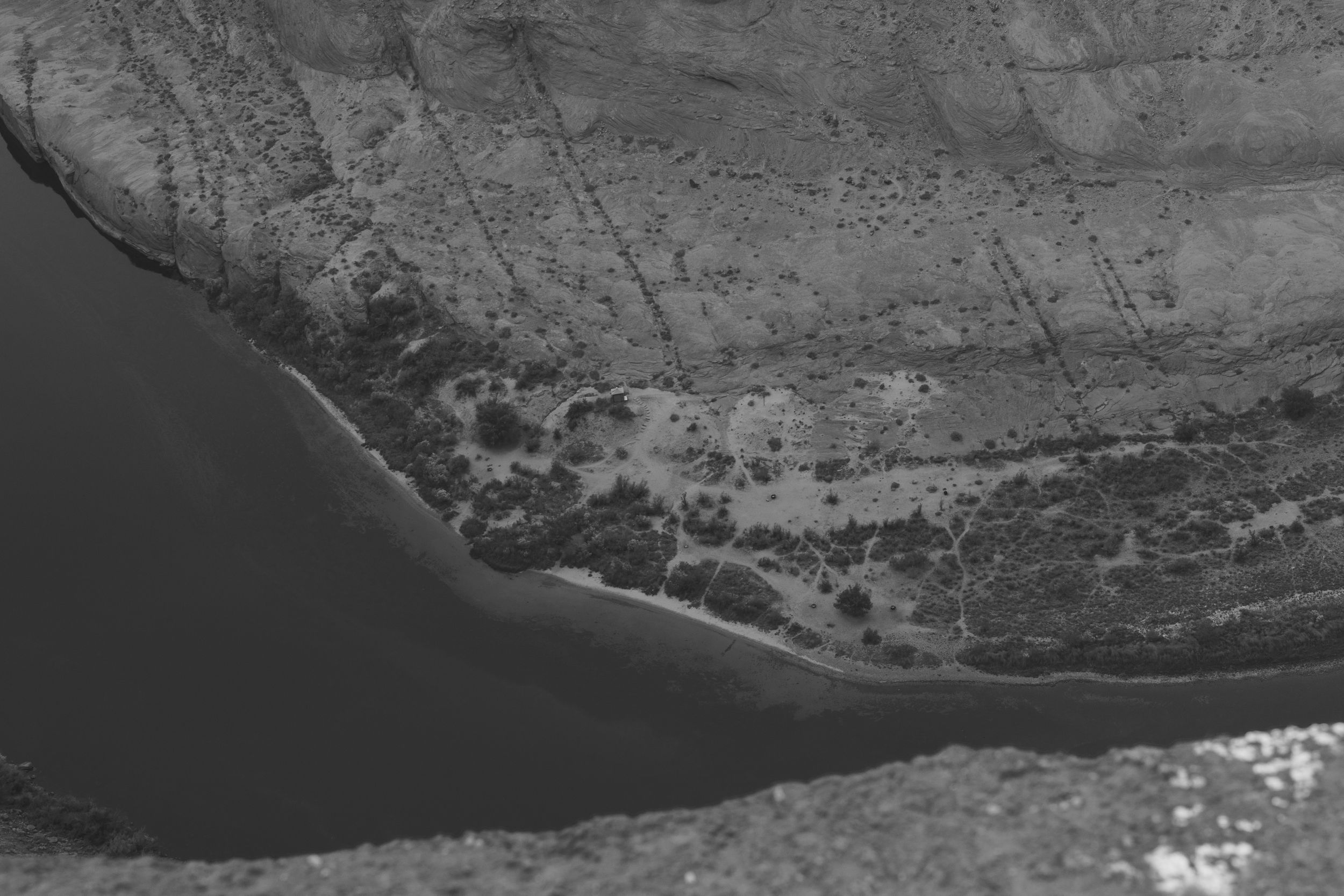 Aerial black and white photograph showing a curved coastline with scattered buildings and vegetation along the shore.