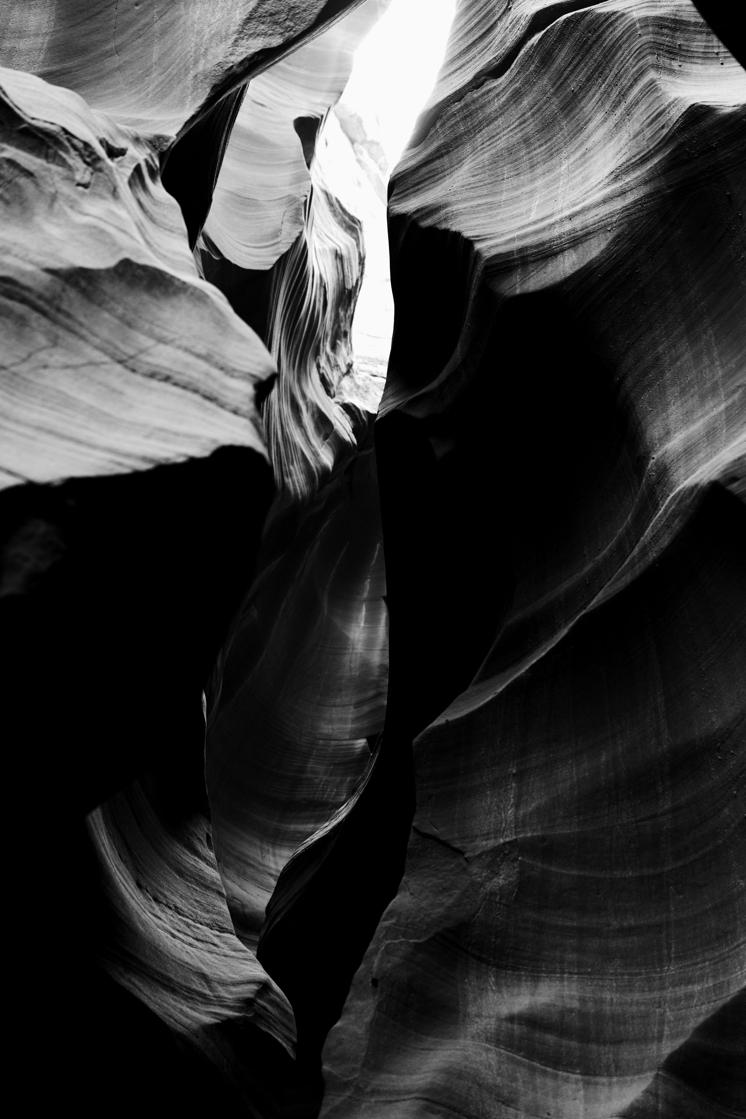 Dramatic black and white view of smooth curved rock formations in Antelope Canyon with light beams streaming down.