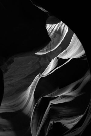 Abstract patterns of light and shadow in a black and white photograph of smooth canyon walls with flowing curves.