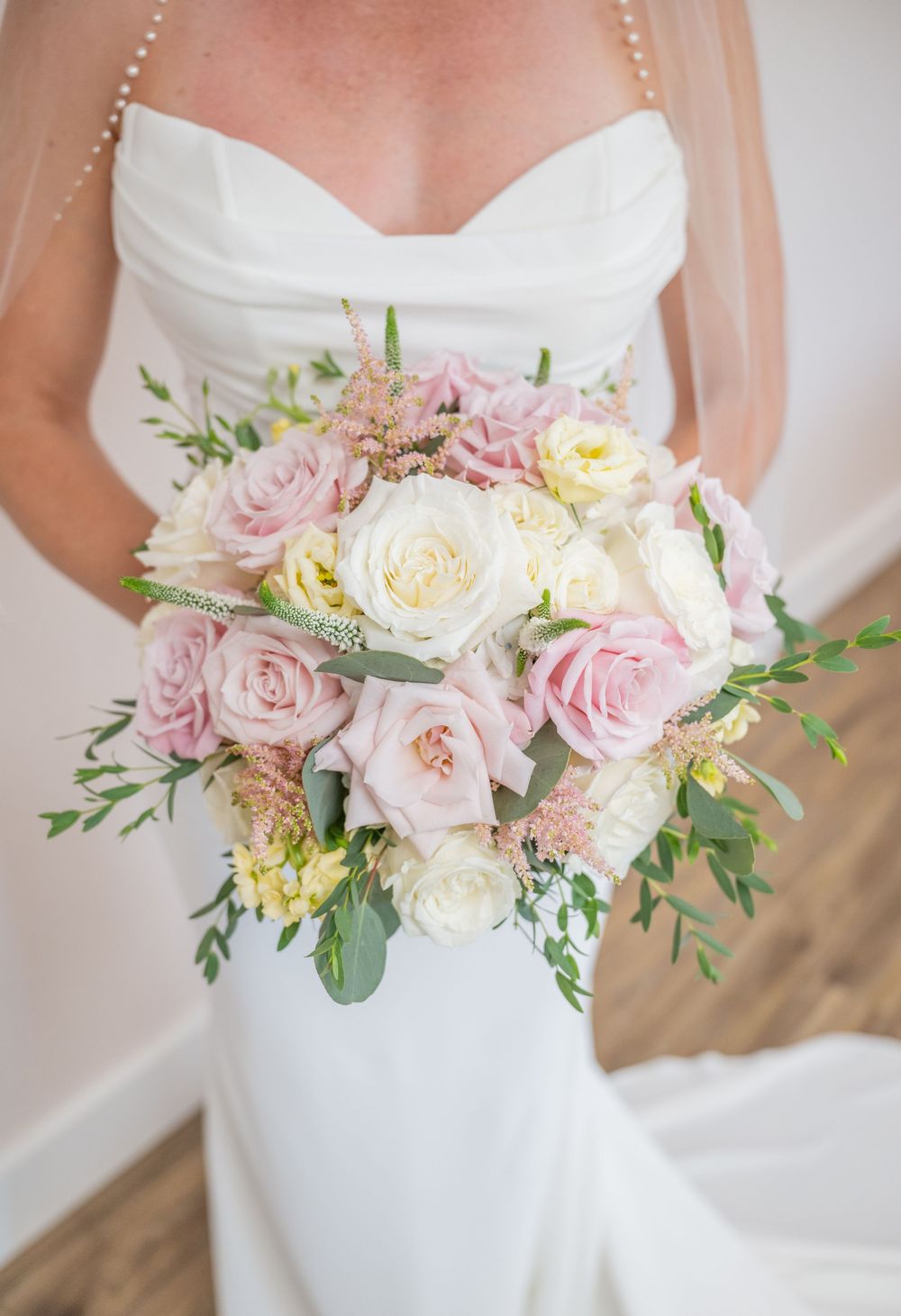 Bride holding a lush cascading bouquet of pink and white roses with greenery in a strapless wedding gown.