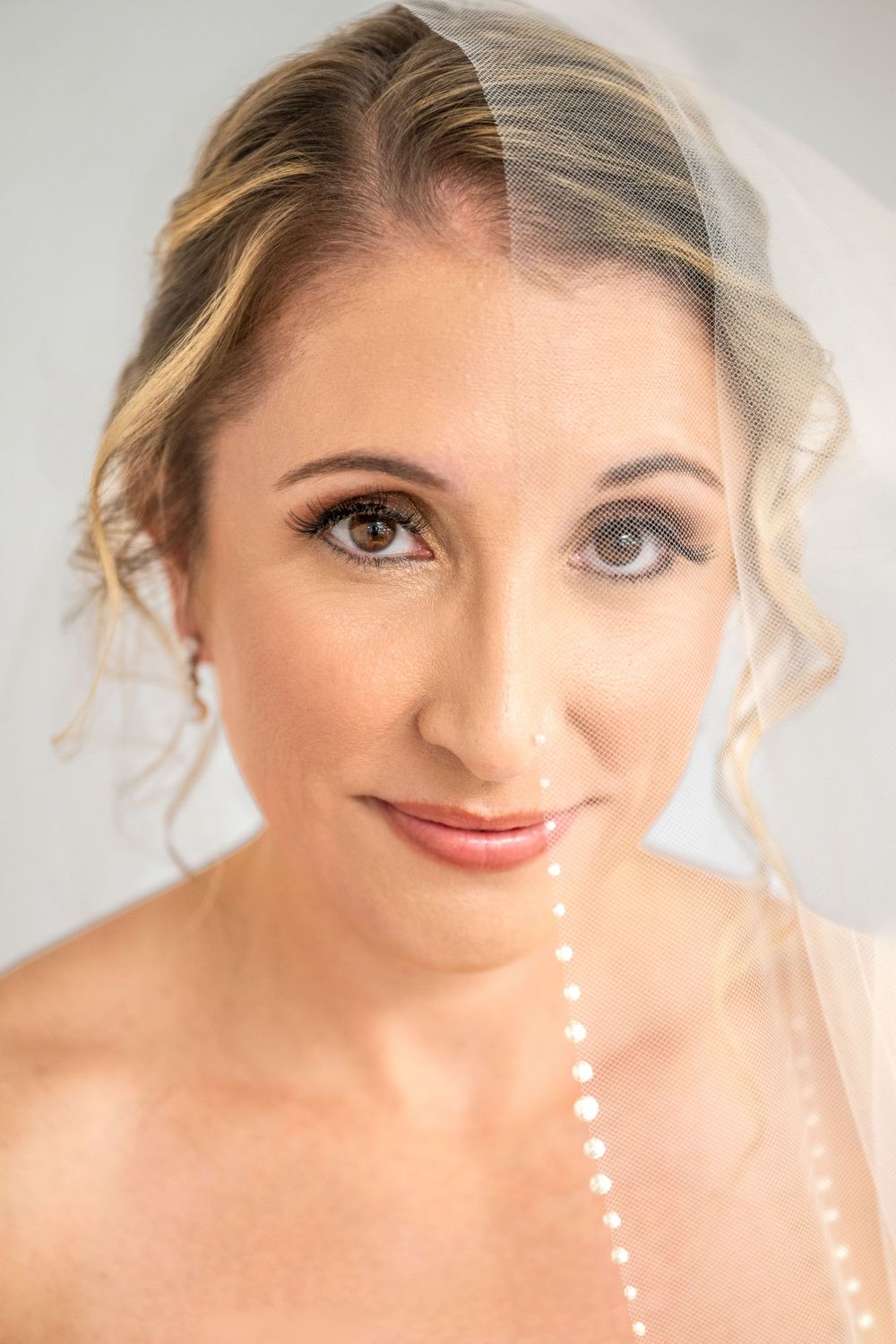 Close-up portrait of a bride wearing a sheer veil and pearl strand, with elegant updo and natural bridal makeup.