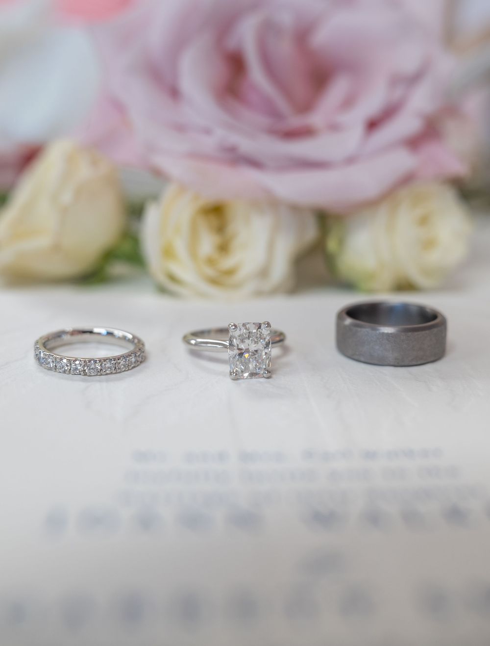 Three wedding rings displayed on an open book with pink roses in the background.
