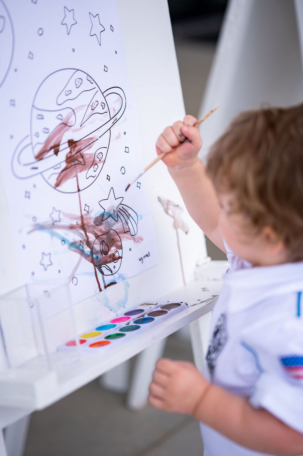 Child painting with watercolors on an easel with stars and space-themed artwork.