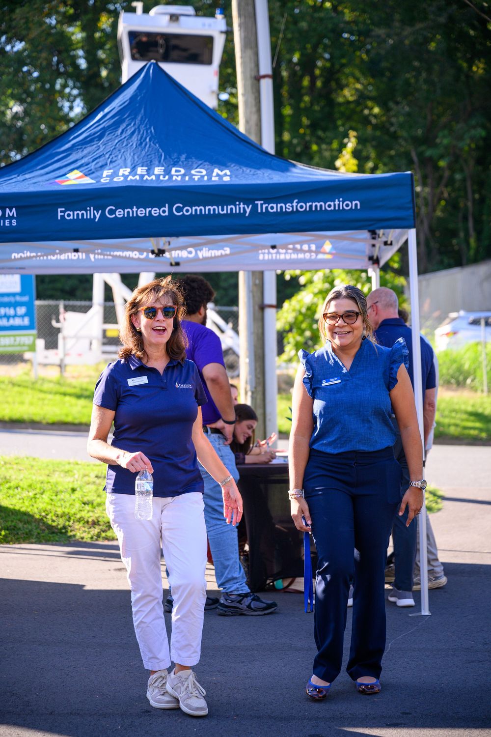 Blue pop-up tents line an outdoor event area while attendees in matching navy shirts gather underneath.
