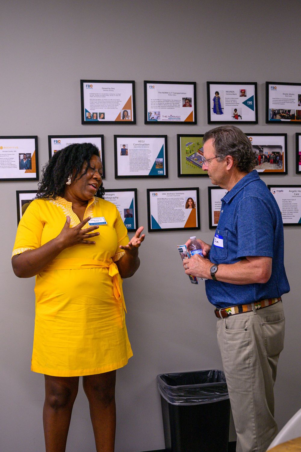 A person in a yellow shirt and shorts interacts with someone in blue during an office conversation.