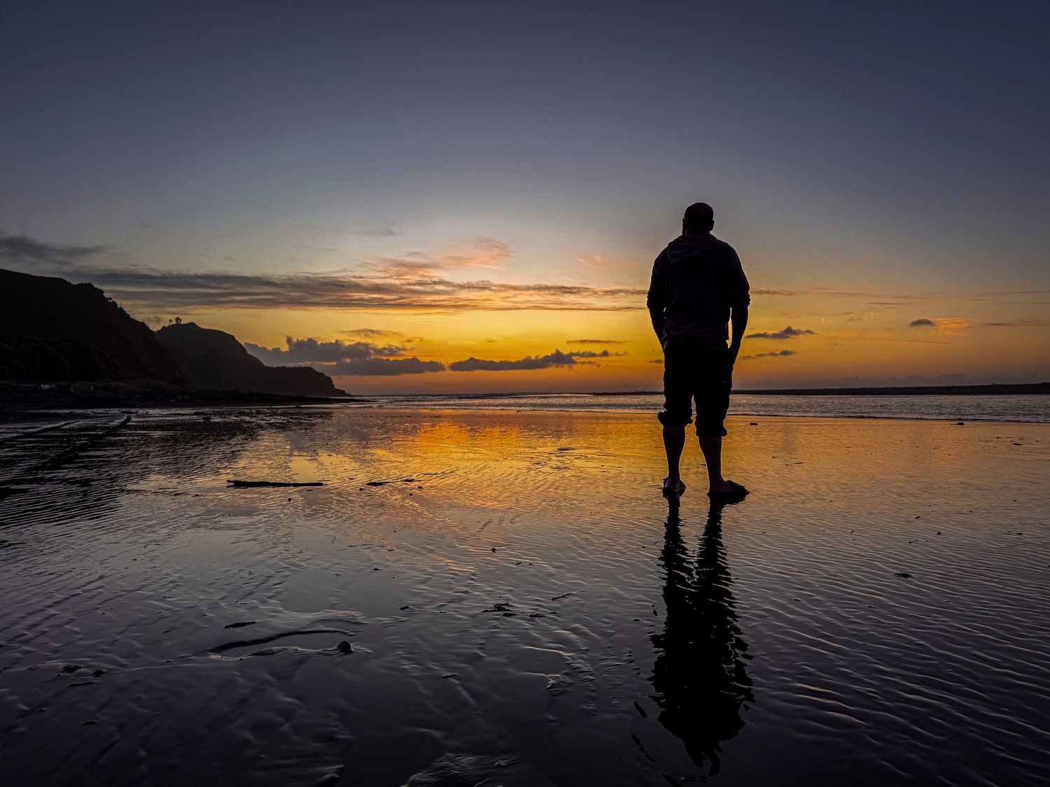 Silhouette reflected on wet beach sand during dramatic coastal sunset.
