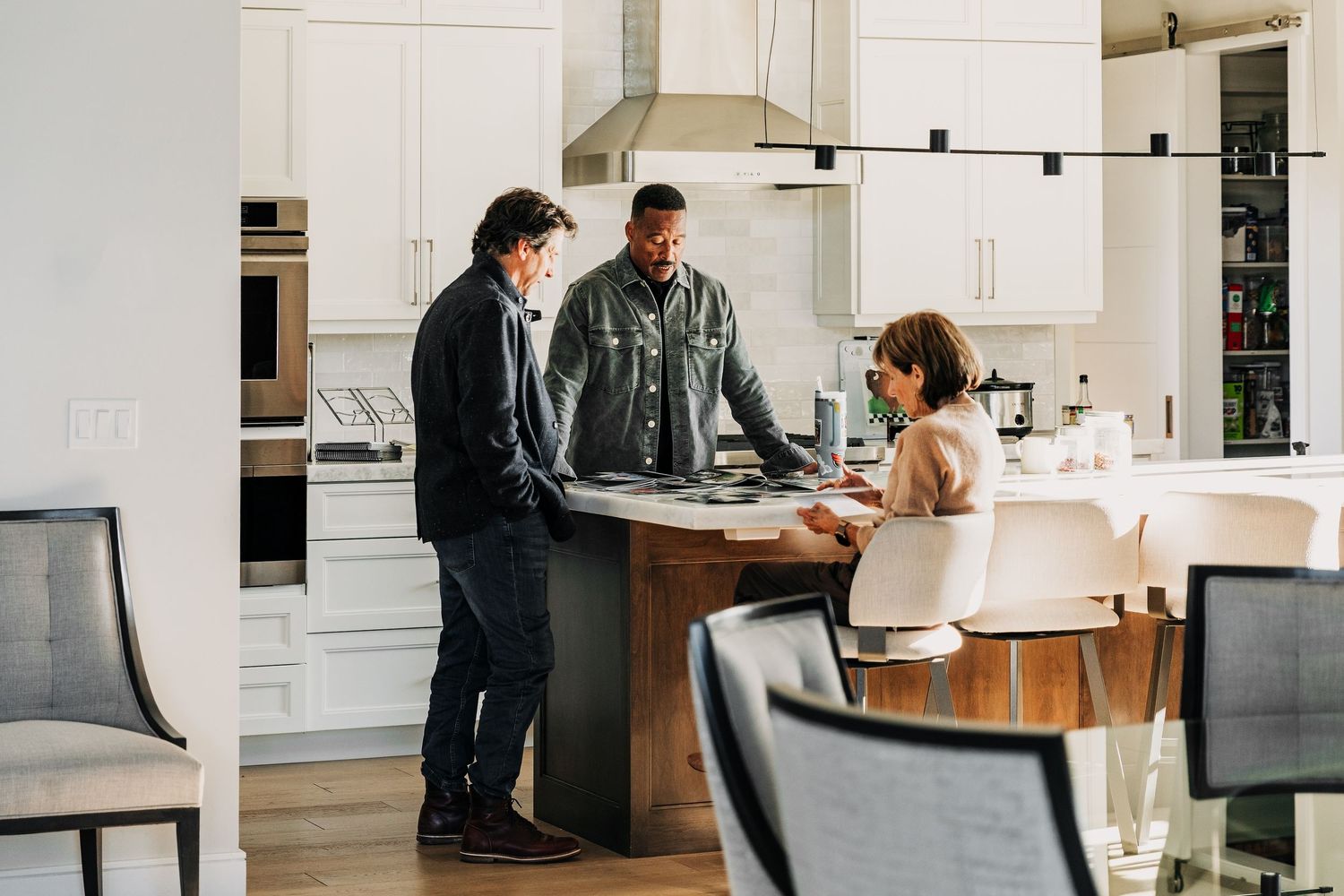 Three people having a discussion around a kitchen island in a modern white kitchen with wood accents.