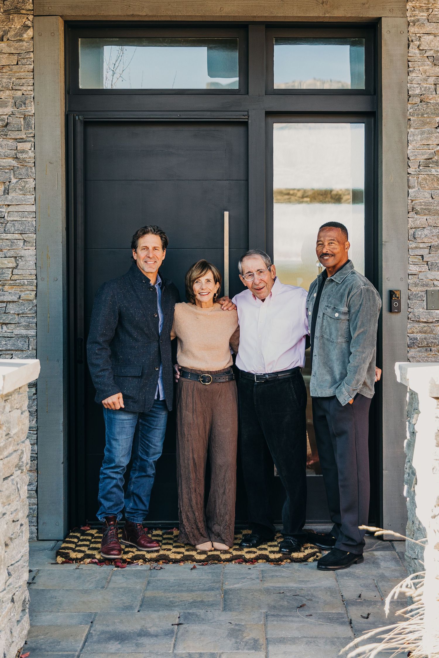 Four smiling adults posing together in front of a modern black front door on a stone home entryway.