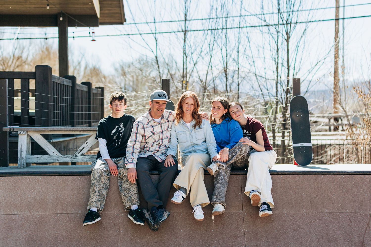 Family of five smiling together on a skate park ledge outdoors on a sunny day.