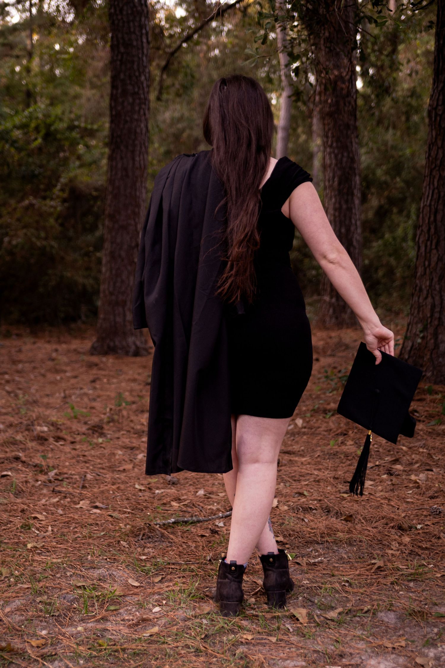 Graduation photoshoot showing black gown details against a wooded background.