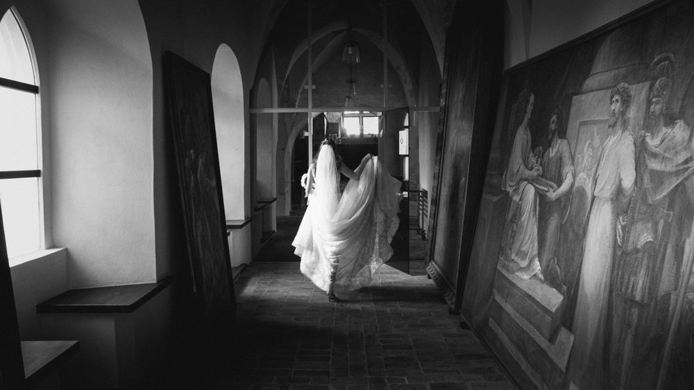 Nuotaka eina pro religinius paveikslus, meniška ir intymi vestuvių akimirka istoriniuose rūmuose Kaune, nespalvota vestuvių fotografija.