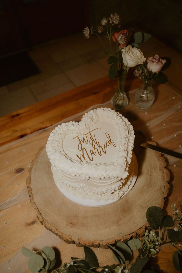 Rustic white wedding cake in a love heart shape displaying 'just marrried' wedding sign on a rustic piece of wood