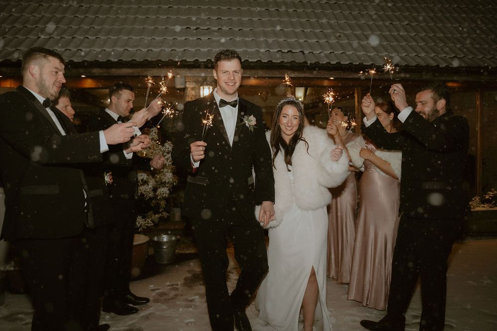 Newlywed couple walking through a sparkler line with guests in formal attire during their wedding celebration in an elegantly decorated venu