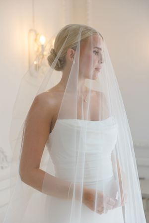 Beautiful side profile of a bride in white gown and veil with soft lighting and candle sconce in background.