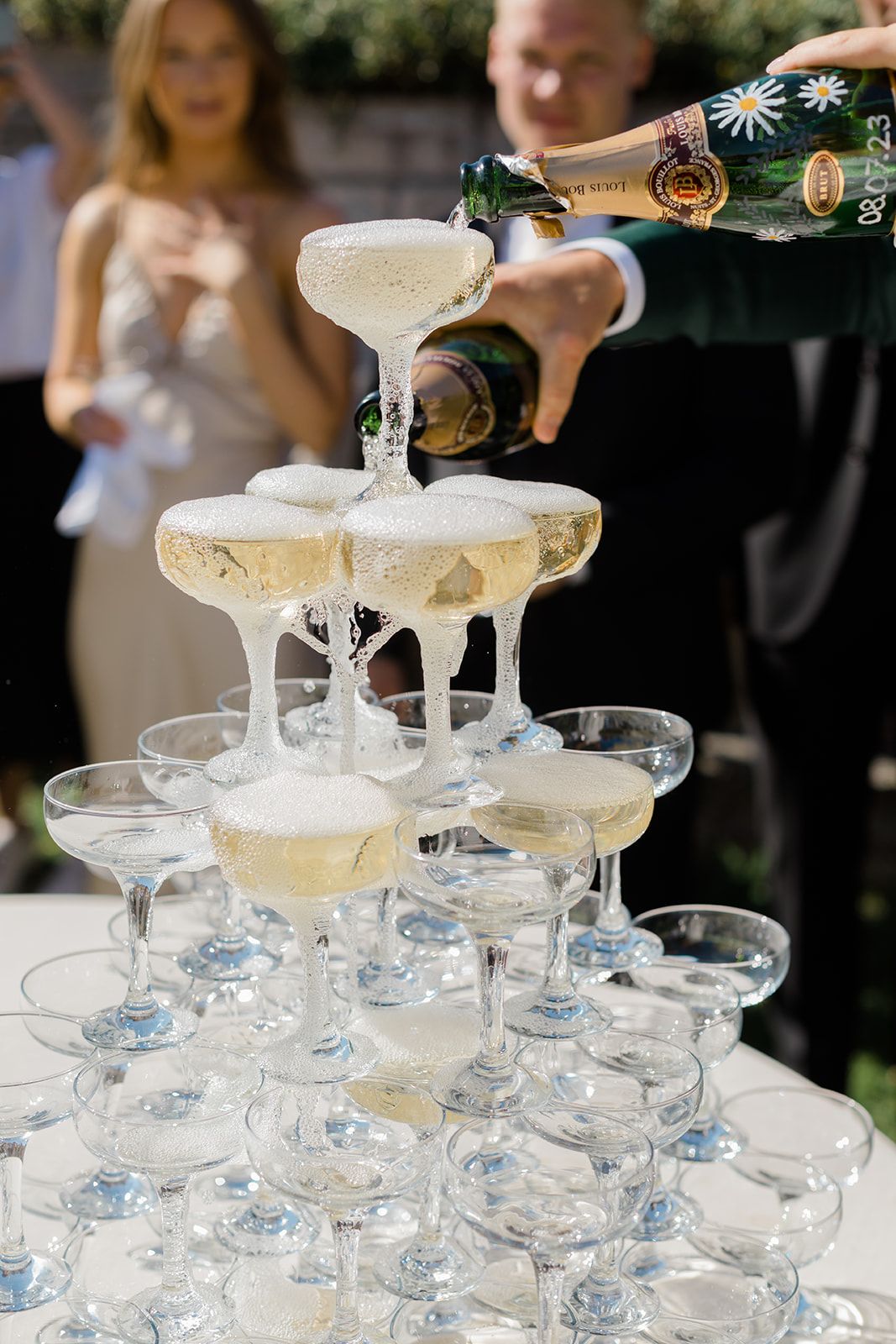 Champagne being poured into a tower of elegant coupe glasses creating a cascading waterfall effect at an event.