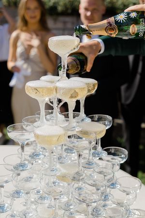 Champagne being poured into a tower of elegant coupe glasses creating a cascading waterfall effect at an event.