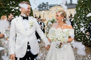 A joyful wedding party celebrates outdoors at an elegant estate venue with white floral bouquets.