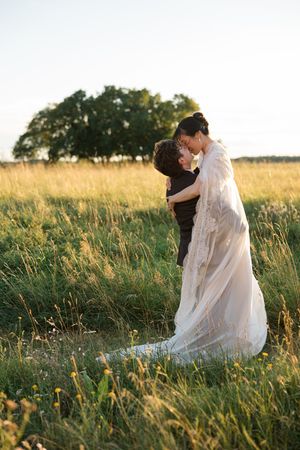 A woman in a flowing white dress sits peacefully in a sunlit meadow of tall grass at golden hour.