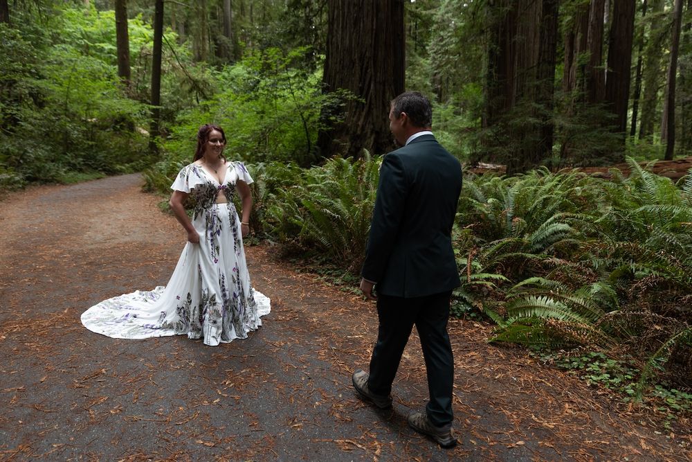 Bride in black and white floral gown with groom in forest redwood wedding ceremony setting.