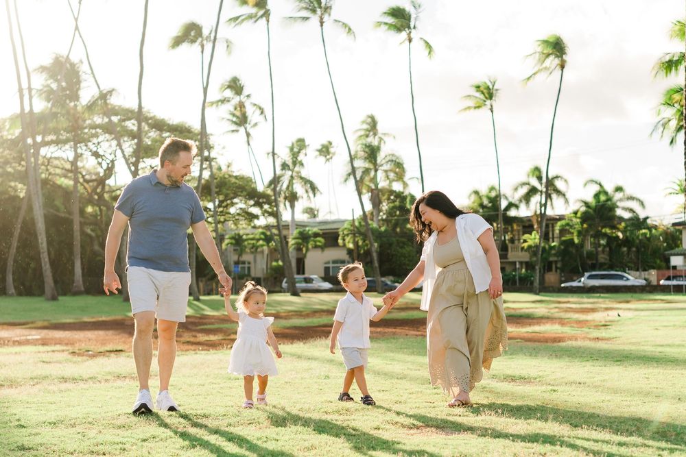 Family enjoying a sunset walk together on a tropical lawn with swaying palm trees in Hawaii.