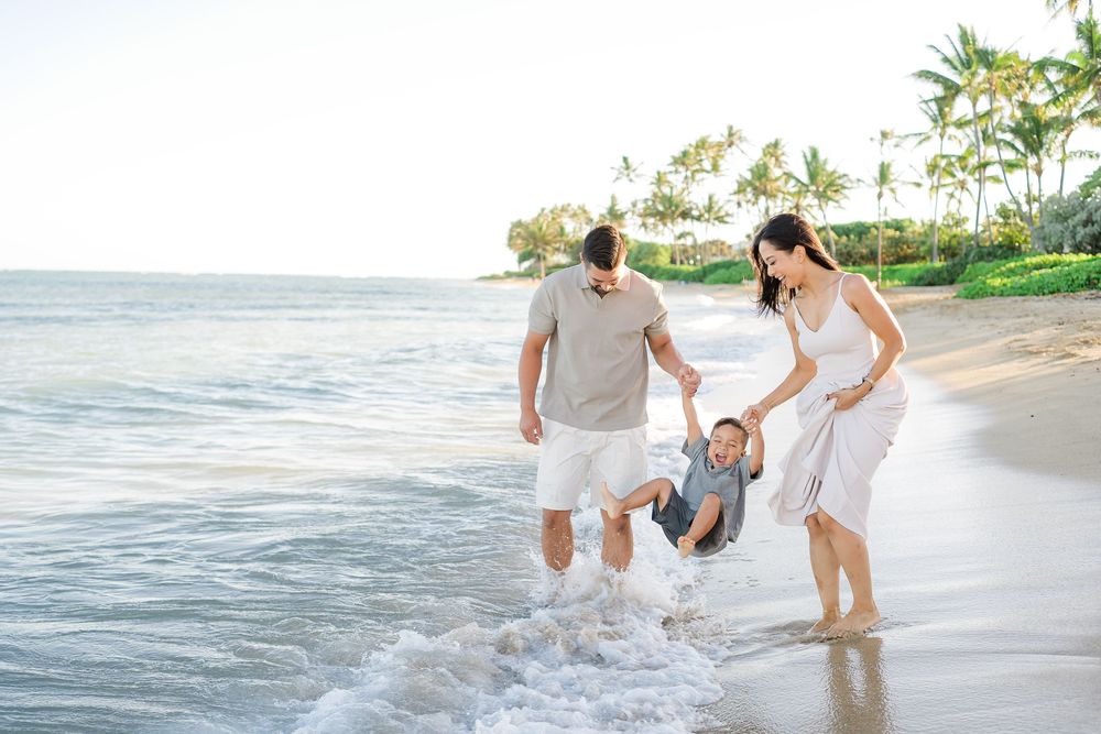 A family in white outfits runs and plays together along a sunny beach shoreline during sunset.