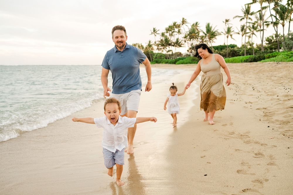 Family enjoying a playful moment running and jumping together on a tropical beach at sunset.