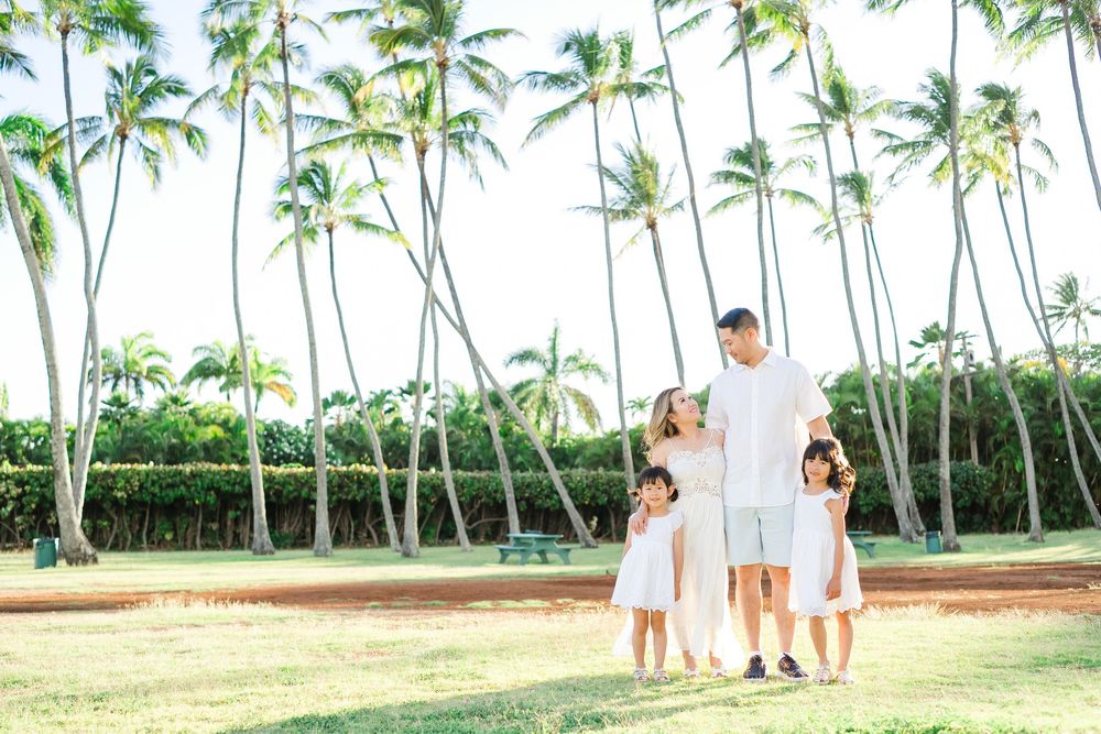 Romantic couple poses for photos surrounded by swaying palm trees on a tropical beach in Hawaii.