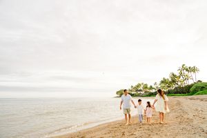 Family walking together on a tropical beach at sunset while holding hands and enjoying the ocean view.