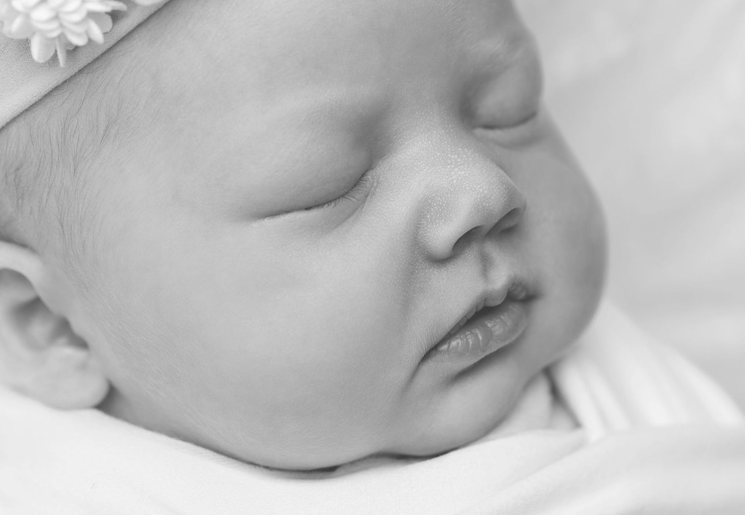 A tender moment captured in black and white as mother kisses sleeping newborn on a wicker chair outdoors.