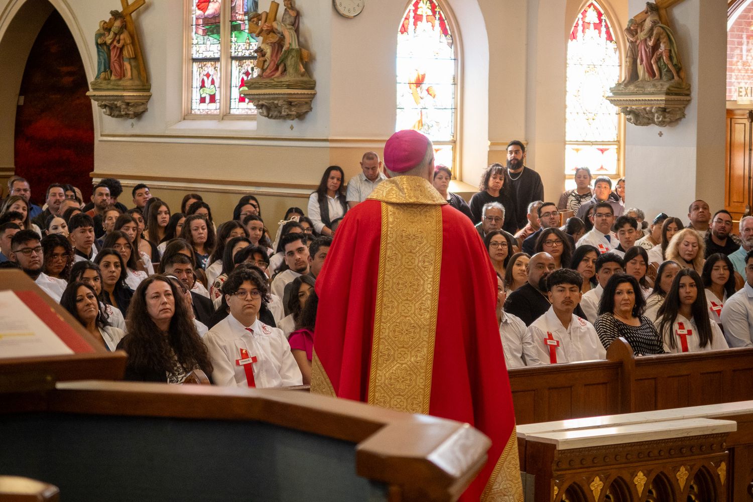 Church congregation gathered in wooden pews during a religious ceremony with stained glass windows visible.